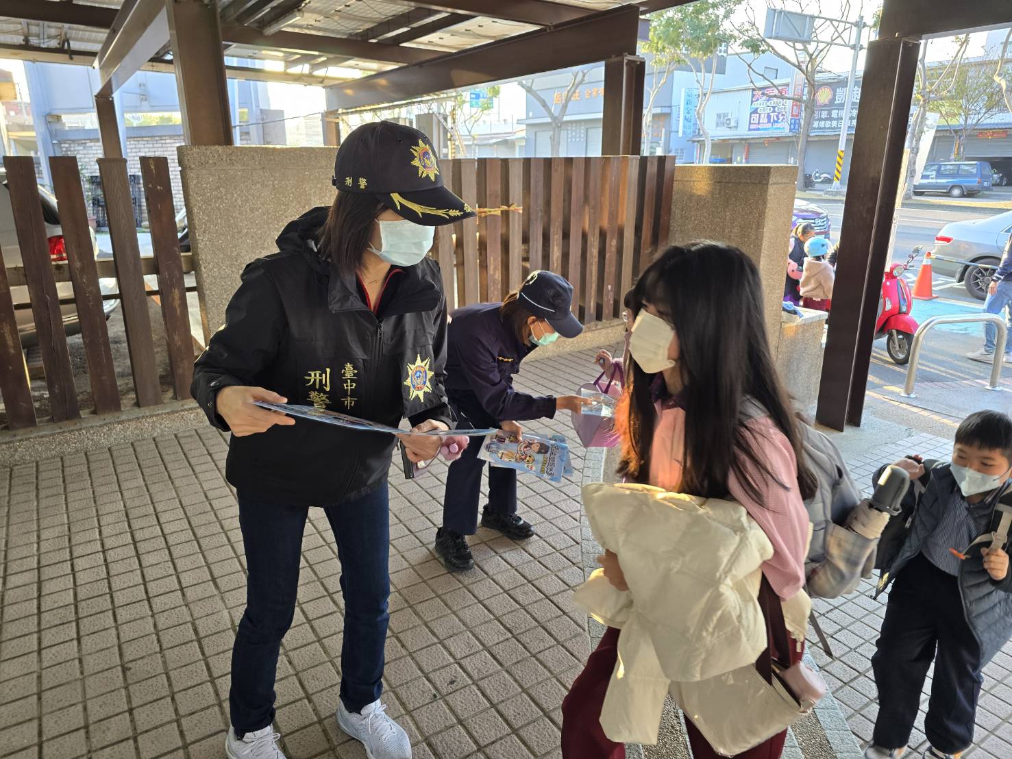 婦幼隊員警在校門口發送墊板和l型資料夾給學童，並提醒自我保護的重要性。